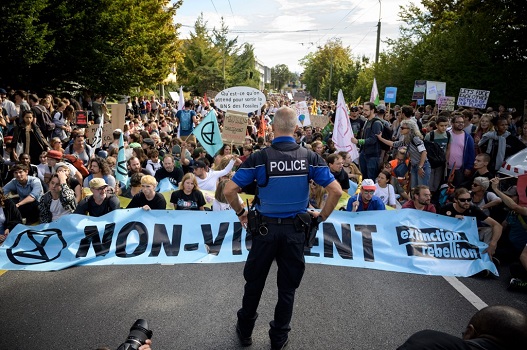 (FILES) In this file photo taken on September 27, 2019 a policeman faces Extinction Rebellion activists during a worldwide climate strike against governmental inaction towards climate breakdown and environmental pollution in Lausanne, western Switzerland. - The ecologist movement Extinction Rebellion (XR), which is expanding rapidly, is organizing action in 60 cities around the world on Monday, including blockading actions in London scheduled to last more than two weeks. (Photo by Fabrice COFFRINI / AFP)