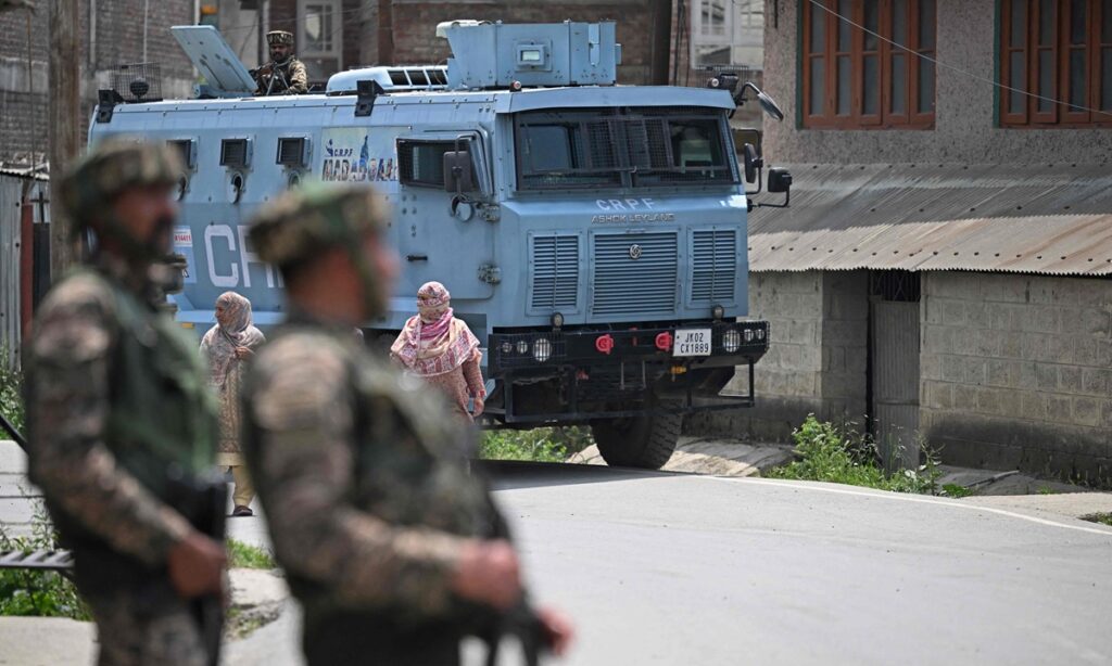 Indian security personnel stand guard as people walk along a road in Wuyan near Srinagar on May 7, 2025, following border tensions. India and Pakistan exchanged heavy artillery fire along their contested frontier on May 7 after New Delhi launched deadly missile strikes on its arch-rival, in the worst violence between the nuclear-armed neighbours in two decades. At least 34 deaths were reported, with Islamabad saying 26 civilians were killed by the Indian strikes and firing along the border, and New Delhi adding at least eight dead from Pakistani shelling. (Photo by Tauseef MUSTAFA / AFP)