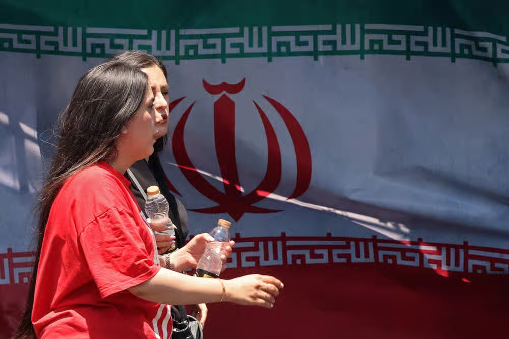 دو زن بی‌حجاب در میدان ونک تهران از کنار پرچم جمهوری اسلامی ایران عبور می‌کنند ـ عکس از خبرگزاری فرانسه.