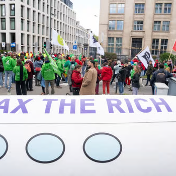 «از ثروتمندان مالیات بگیرید» (Tax The Rich)، شعار سازمان «آکسفام» (Oxfam) در تظاهرات علیه افزایش قیمت انرژی در بروکسل (بلژیک) که سه اتحادیهٔ‌ کارگری برگزار کردند. ۱۲ مه ۲۰۲۶ ـ عکس از خبرگزاری فرانسه.