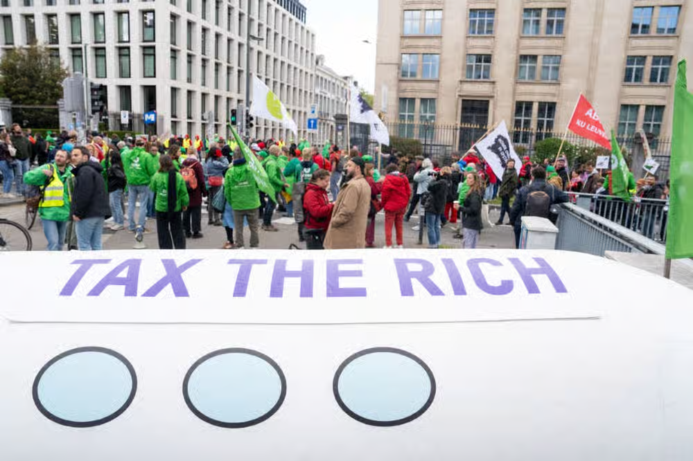 «از ثروتمندان مالیات بگیرید» (Tax The Rich)، شعار سازمان «آکسفام» (Oxfam) در تظاهرات علیه افزایش قیمت انرژی در بروکسل (بلژیک) که سه اتحادیهٔ‌ کارگری برگزار کردند. ۱۲ مه ۲۰۲۶ ـ عکس از خبرگزاری فرانسه.